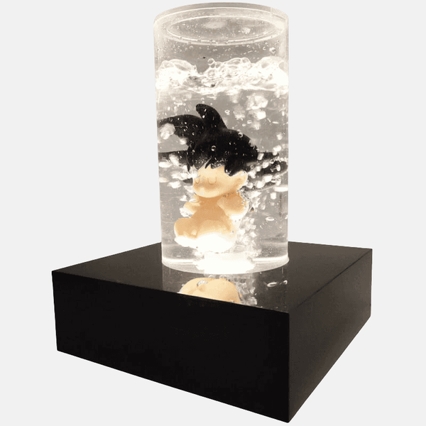 Vue de profil de la figurine Baby Goku 18cm dans sa capsule, montrant le socle noir et le système d'éclairage LED.